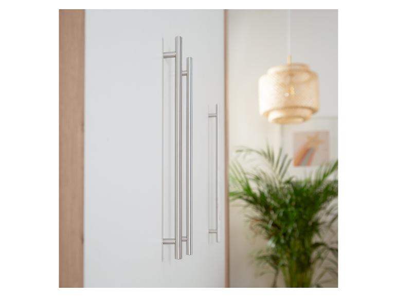 Weiße Schranktüren mit langen, schlanken Metallgriffen in einem hellen Raum mit Hängelampe und Pflanze.