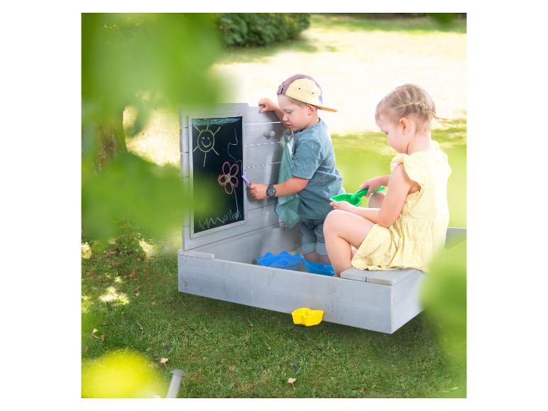 Kinder spielen mit einem Holzsandkasten mit Tafel im Garten.
