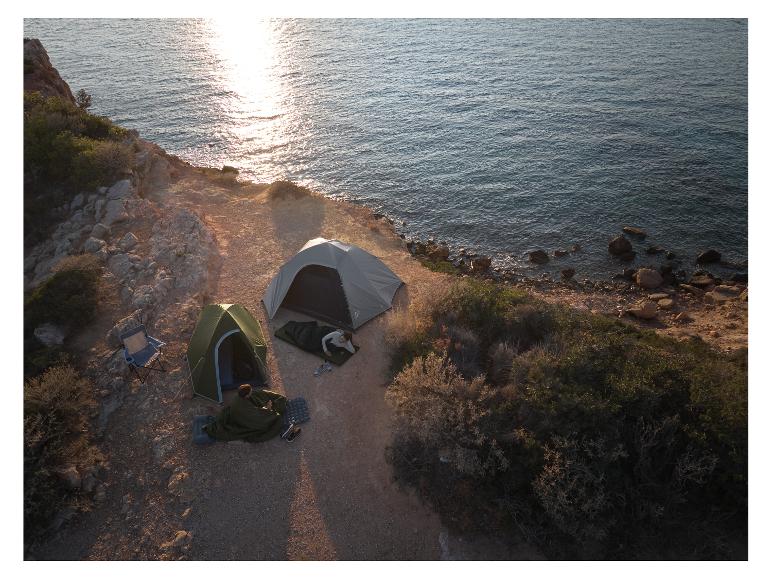 Zwei Campingzelte und zwei Personen, die am Meer bei Sonnenuntergang entspannen.