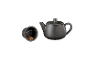 Schwarze Teekanne aus Keramik mit Teesieb auf schwarzem Hintergrund.