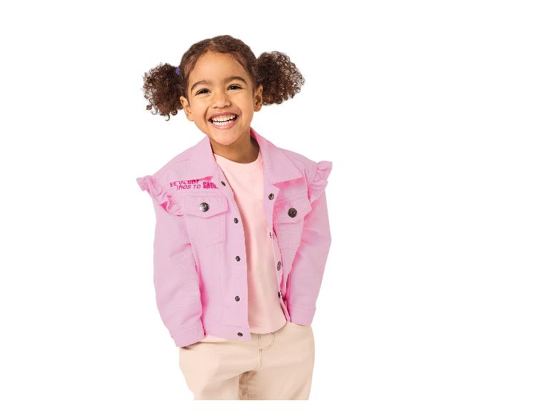 Lächelndes Mädchen in rosa Jeansjacke mit Rüschen und beiger Hose.