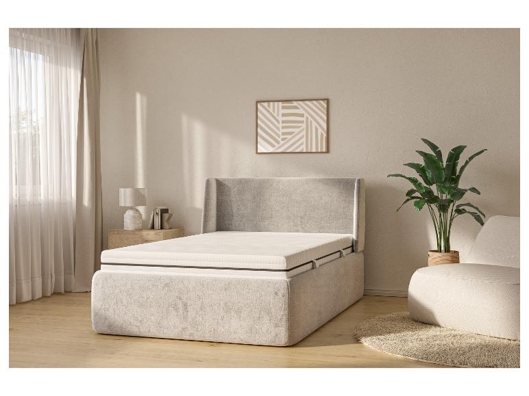 Helles Schlafzimmer mit beigem Polsterbett, Nachttisch, Lampe und Pflanze.