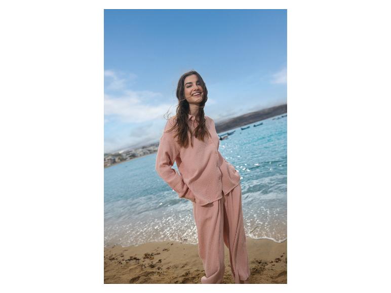 Lächelnde Frau in rosa Outfit am Strand mit Meer im Hintergrund.