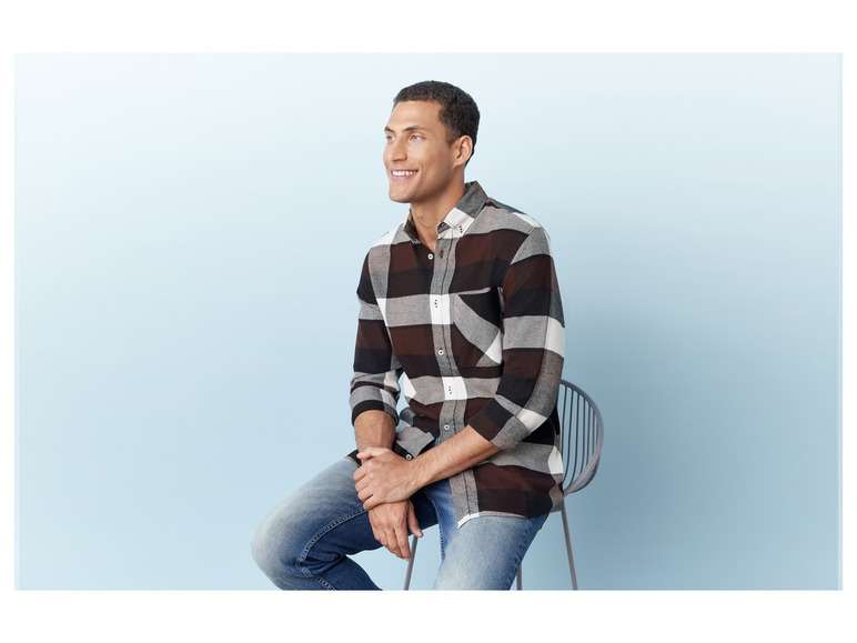 Mann in einem karierten Hemd und Jeans sitzt auf einem Stuhl.