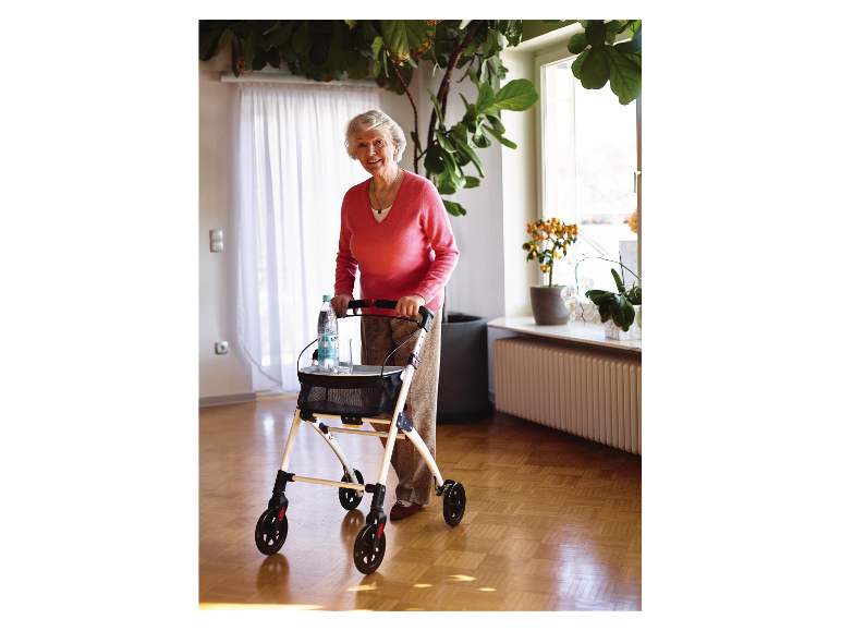 Eine lächelnde ältere Frau benutzt einen Rollator mit einer Wasserflasche.