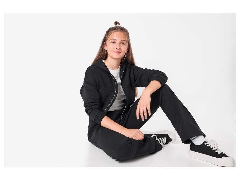 Mädchen in schwarzem Kapuzenpullover und Jogginghose sitzt auf dem Boden