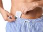 Ein Mann legt eine Damenbinde in eine blau-weiß gestreifte Badehose.