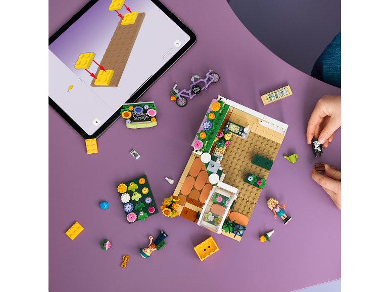 Blick von oben auf eine Person, die einen Spielzeug-Blumenladen mit einer Anleitung auf einem Tablet baut.