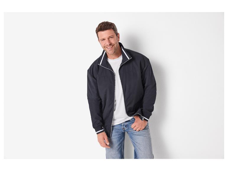 Lächelnder Mann in einer dunkelblauen Jacke, weißem T-Shirt und Jeans.