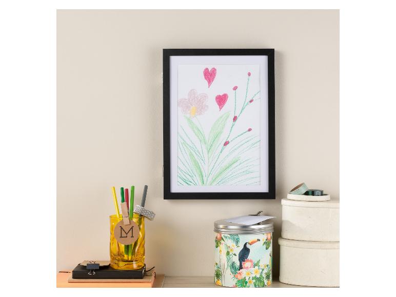 Ein gerahmtes Bild mit Blumen, Bleistifte in einem Behälter, eine Dose mit einem Tukan und zwei runde Dosen.