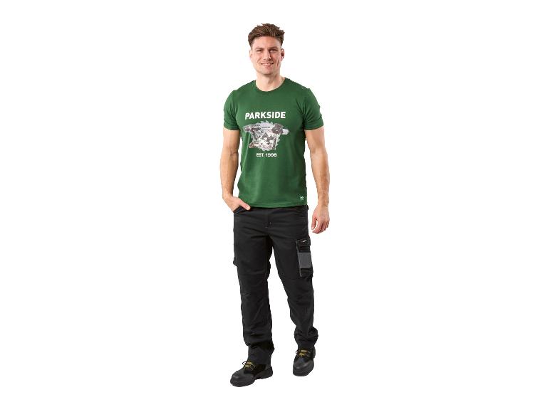 Mann in grünem T-Shirt mit Werkzeugaufdruck und schwarzer Arbeitshose.