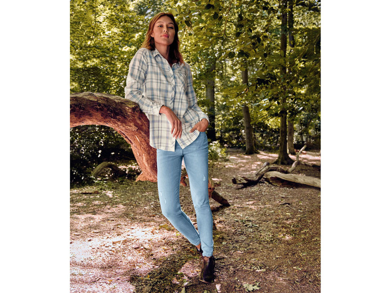 Eine Frau in einem karierten Hemd und blauen Jeans posiert in einem Wald.