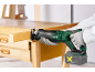 Eine Person mit Handschuhen benutzt eine Akku-Säbelsäge, um einen Holzbalken auf einer Werkbank zu schneiden.