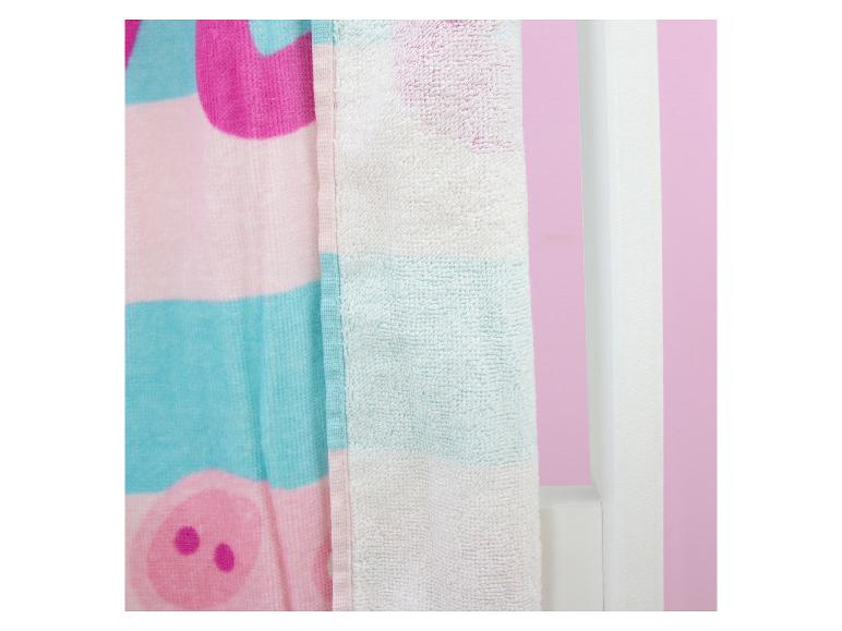 Rosa-blaues Handtuch mit Schweinchenmuster, hängt an einer weißen Wand.