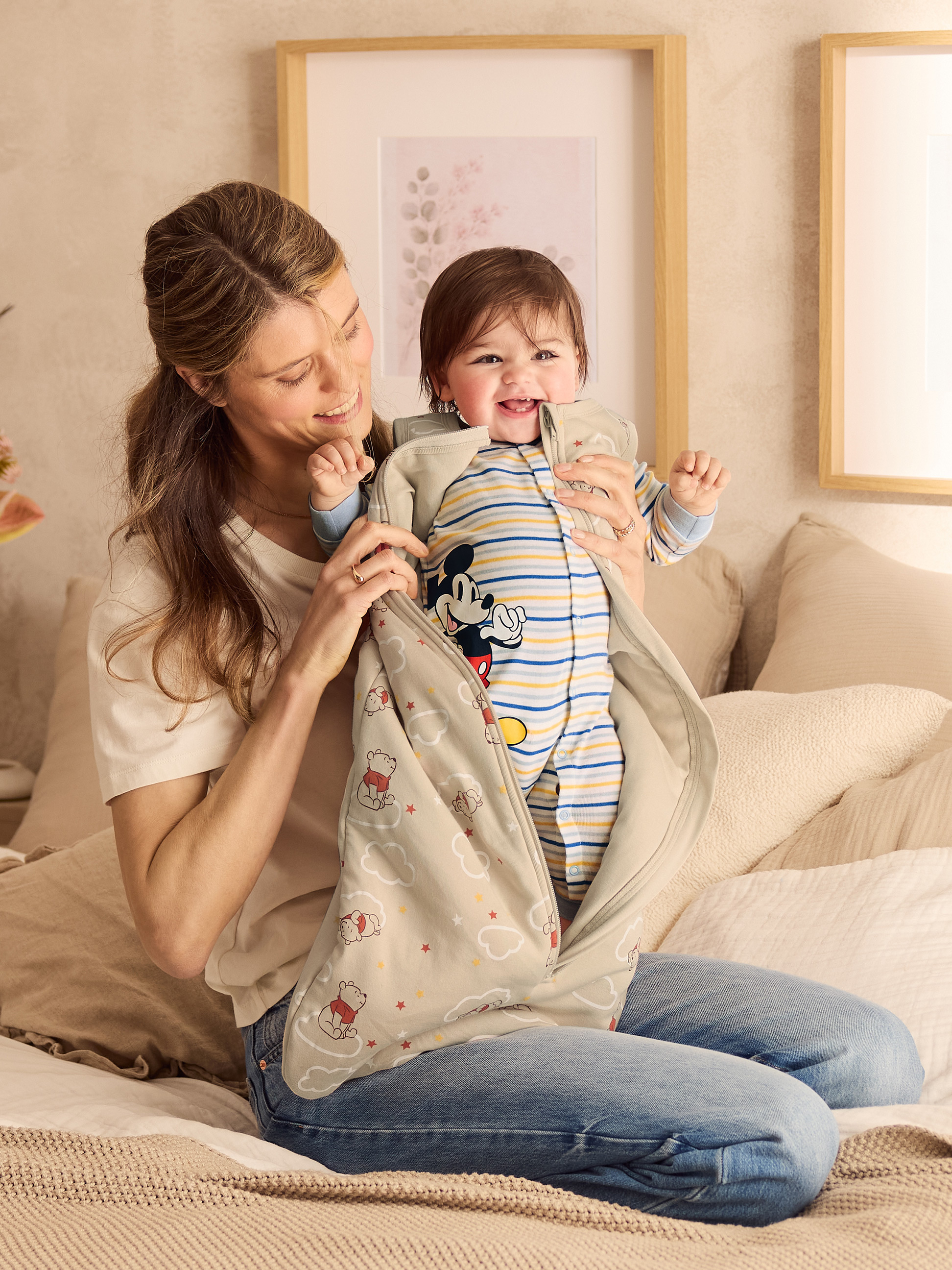 Lächelnde Mutter hält lachendes Baby in Winnie Puuh-Schlafsack.