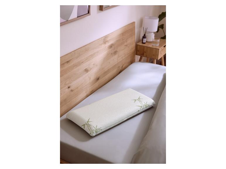 Weißes Kissen mit Bambusmuster auf einem Bett mit Holz-Kopfteil und Nachttisch.