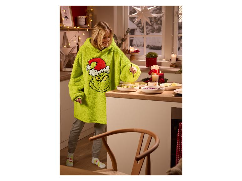 Frau in einem übergroßen Grinch-Hoodie bereitet Essen in einer weihnachtlich dekorierten Küche zu.