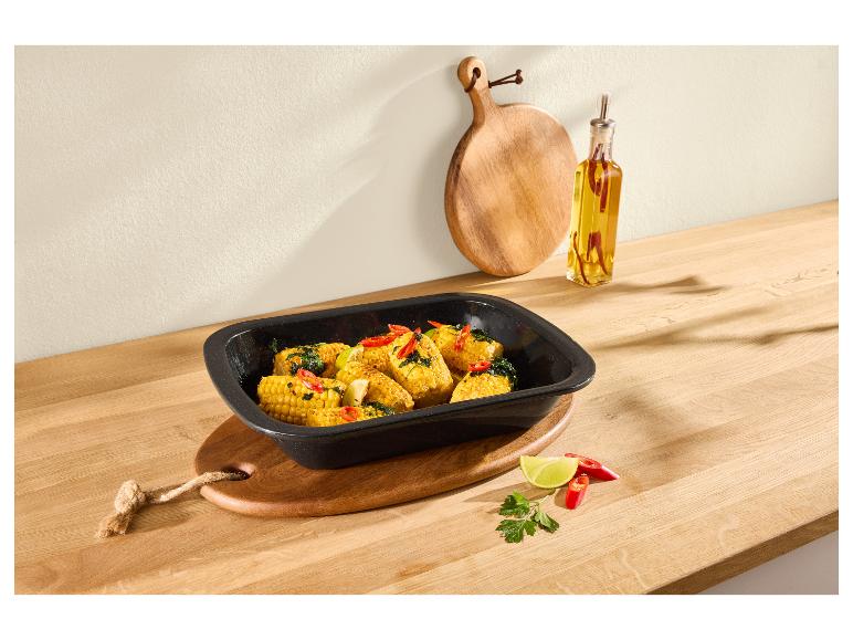 Gebratener Maiskolben mit Chili und Limette in einer schwarzen Auflaufform auf einer Holztheke.