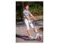 Lächelndes Mädchen auf einem Roller, trägt ein gestreiftes T-Shirt und weiße Hosen.