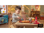 Kleiner Junge schneidet Spielzeugpizza mit Spielzeugbesteck an einem Holztisch in einem Kinderzimmer.