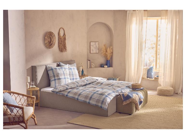 Gemütliches Schlafzimmer mit Bett in karierter Bettwäsche, Korbsessel und Boho-Dekor.