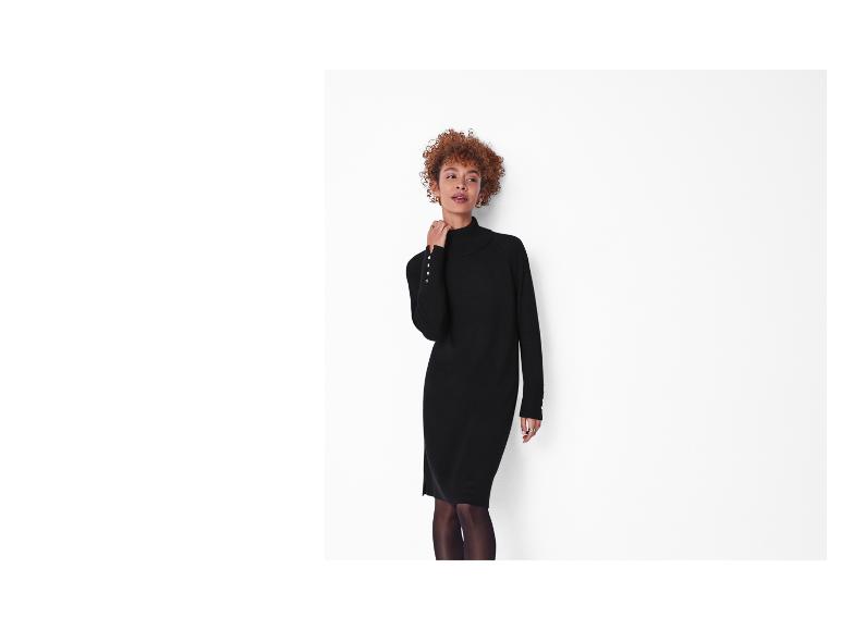 Frau in einem schwarzen Strickkleid mit Rollkragen und Knöpfen an den Ärmeln.