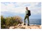 Frau mit Rucksack und sportlicher Wanderkleidung auf einer Klippe mit Meerblick.