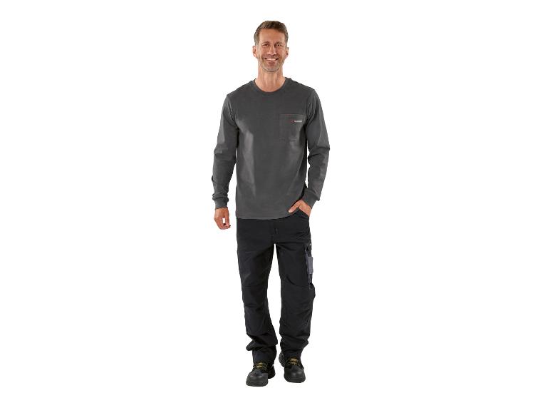 Lächelnder Mann in grauem Langarmshirt und schwarzer Arbeitshose