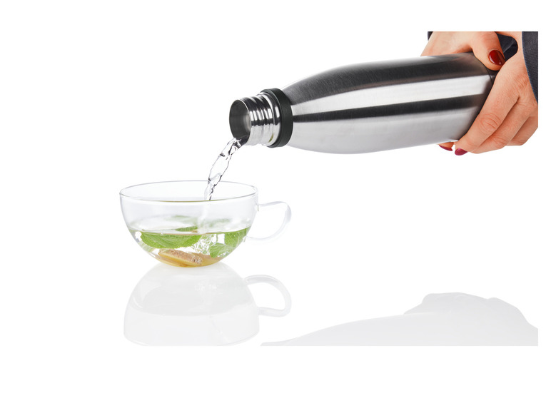 Eine Thermoskanne gießt Wasser in eine Tasse mit Minze und Ingwer.