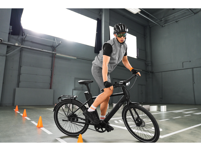 Mann auf einem E-Bike mit Helm und Brille, fährt in Innenräumen.