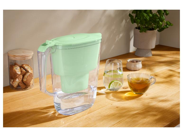 Wasserfilterkanne, Glas Wasser mit Limette und Teetasse auf einem Holztisch.