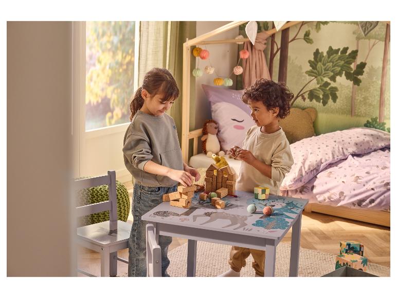 Zwei Kinder spielen mit Bauklötzen und Spielzeug an einem Kindertisch mit Waldmotiv.