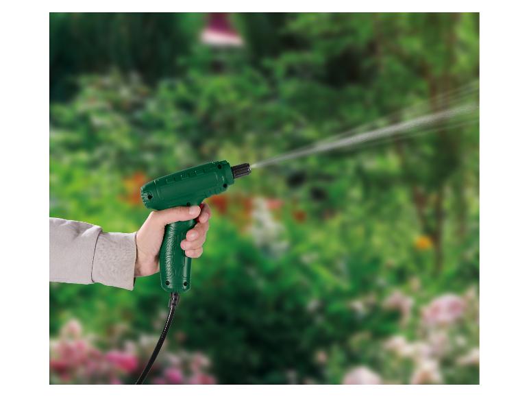 Handgehaltene grüne Sprühpistole, die Wasser in einen grünen Garten sprüht.