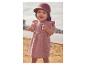 Baby in einem rosa Kleid und Sonnenhut, am Sandstrand stehend.