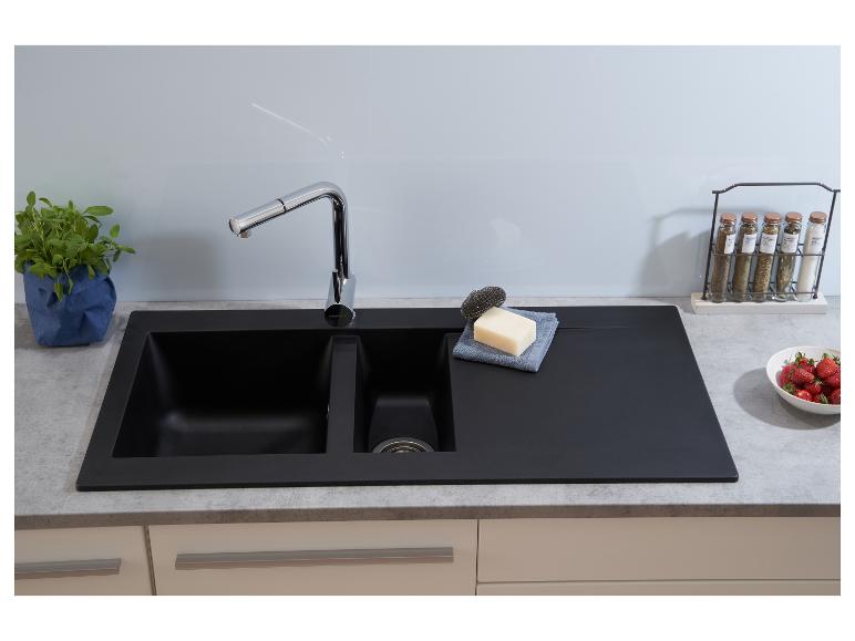 Schwarze Küchenspüle mit Wasserhahn, Seife, Schwamm und Gewürzen auf der Arbeitsplatte.