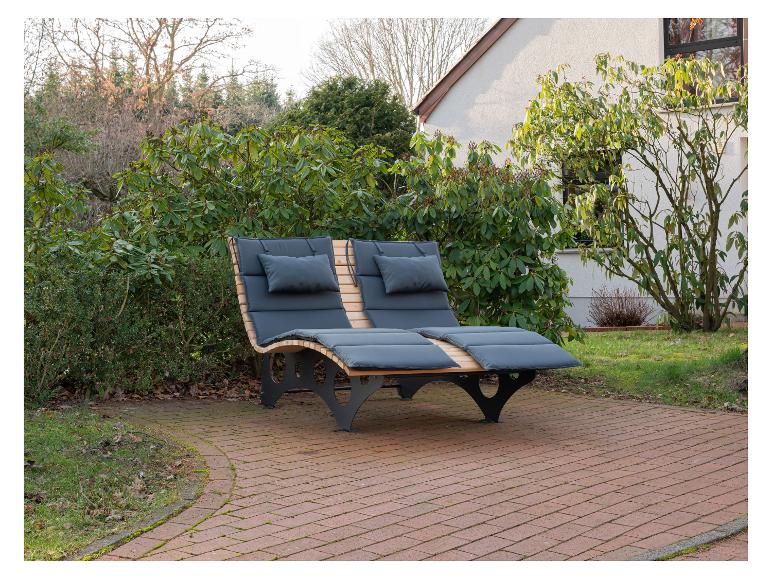 Holzliege mit dunkelgrauen Polstern auf einer Terrasse im Garten.