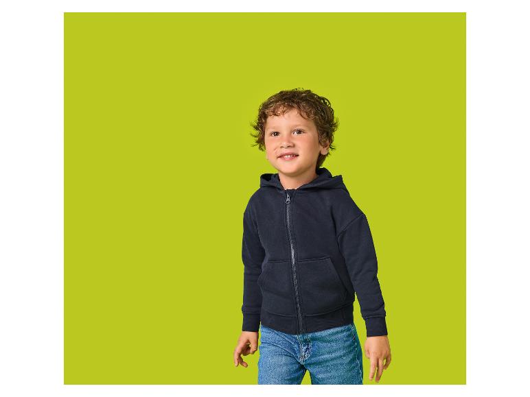 Lächelnder Junge mit Locken, dunkelblauem Kapuzenpullover und Jeans.