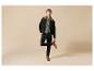 Mann in dunkelgrüner Jacke, hellgrünem Pullover, schwarzer Hose und braunen Stiefeln.