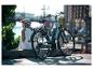 Frau mit Helm sitzt neben einem E-Bike mit Stadt- und Wasserhintergrund.