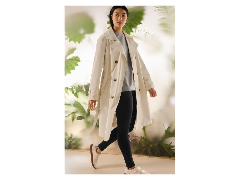 Frau in beigem Trenchcoat, hellgrauem Top, schwarzen Leggings und weißen Sneakern.