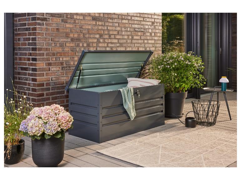 Dunkelgraue Gartenaufbewahrungsbox mit offenem Deckel, Kissen und Decke auf einer Terrasse.