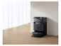 Schwarzer Saugroboter mit Ladestation in einem Raum mit weißen Vorhängen und Holzboden.