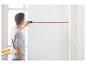 Mann verwendet eine Laserwasserwaage, um eine horizontale Linie an eine weiße Wand zu projizieren.
