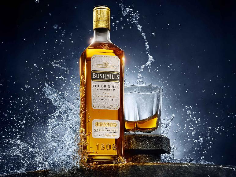 Flasche irischer Whiskey und ein Glas mit Whiskey, umgeben von spritzendem Wasser.