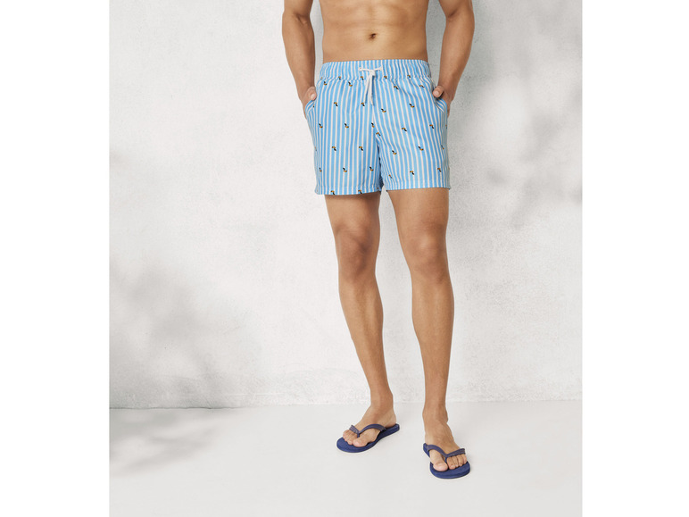 Ein Mann trägt blaue, gestreifte Badehosen und Flip-Flops.