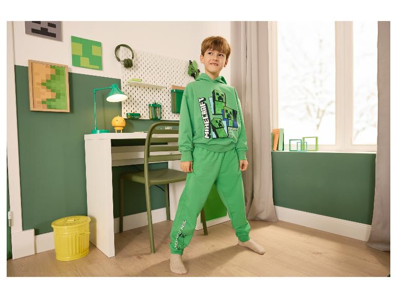 Junge in grünem Minecraft-Trainingsanzug in einem Zimmer mit thematischer Dekoration.