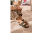 Grüne Herren-Sandalen mit Schnallen, beigefarbene Hose und grünes T-Shirt, auf einem Teppich sitzend.
