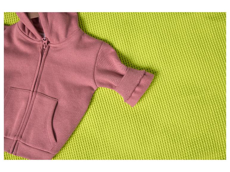 Rosa Kapuzenpullover auf einer strukturierten lindgrünen Decke.