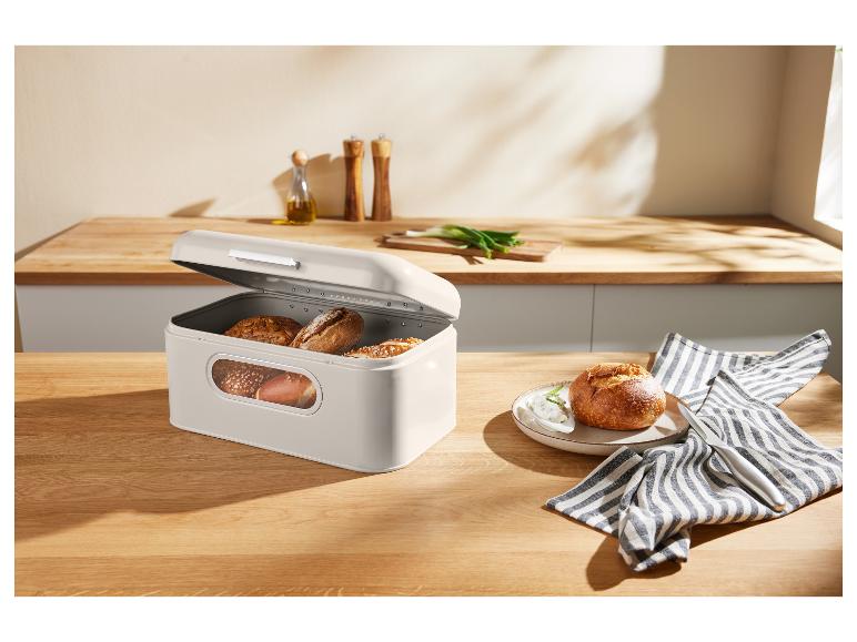 Ein beiger Brotkasten mit Brot auf einem Holztisch in einer Küche.