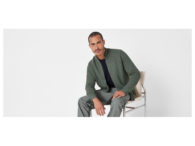 Mann in einer grünen Jacke und Hose sitzt auf einem Stuhl.